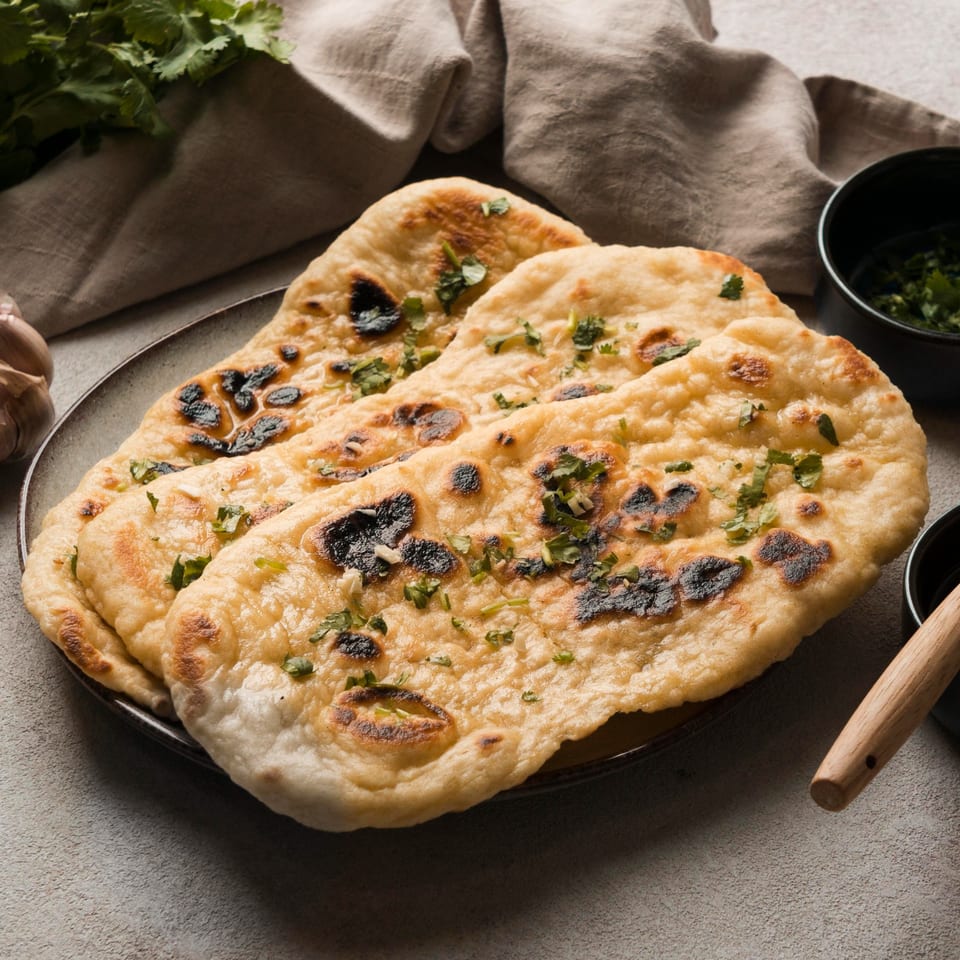 Two pieces of Nepalese garlic naan bread, garnished with cilantro, on a dark plate.