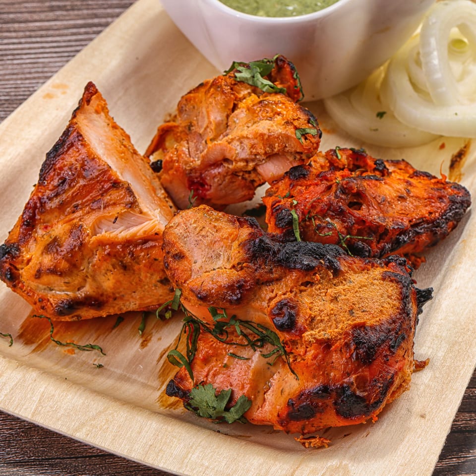 Nepalese chicken tikka, garnished with cilantro, served with sliced onions and green chutney.