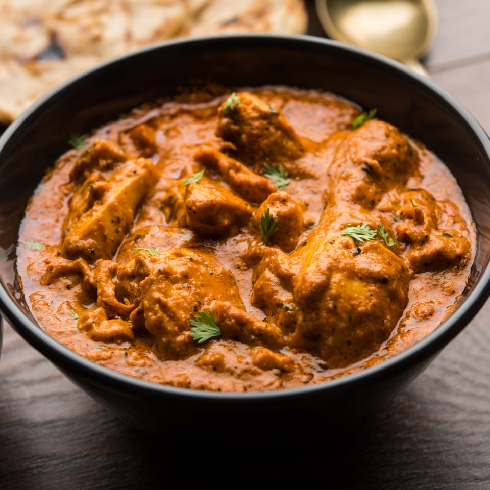 Close-up of a black bowl filled with rich, orange Nepalese curry, garnished with fresh cilantro.