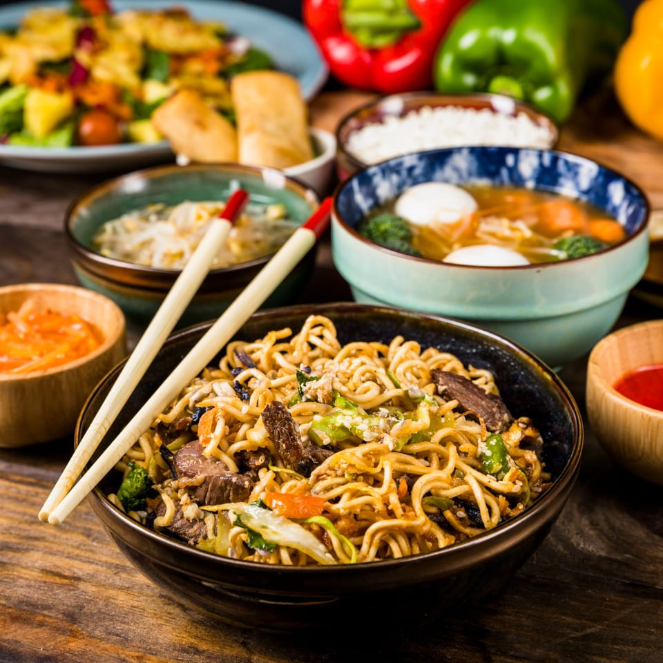 Nepalese stir-fried noodles with beef and vegetables, surrounded by other dishes and bell peppers.
