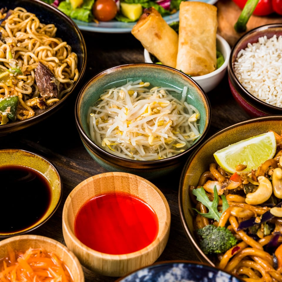 Assortment of Nepalese dishes including noodles, rice, spring rolls, bean sprouts, and sauces.