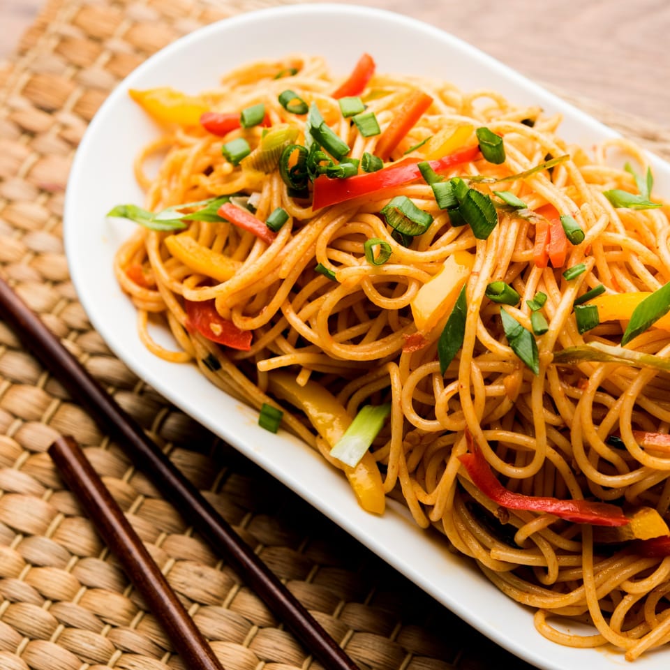 Nepalese Chowmein noodles with colorful bell peppers and green onions, served with chopsticks.
