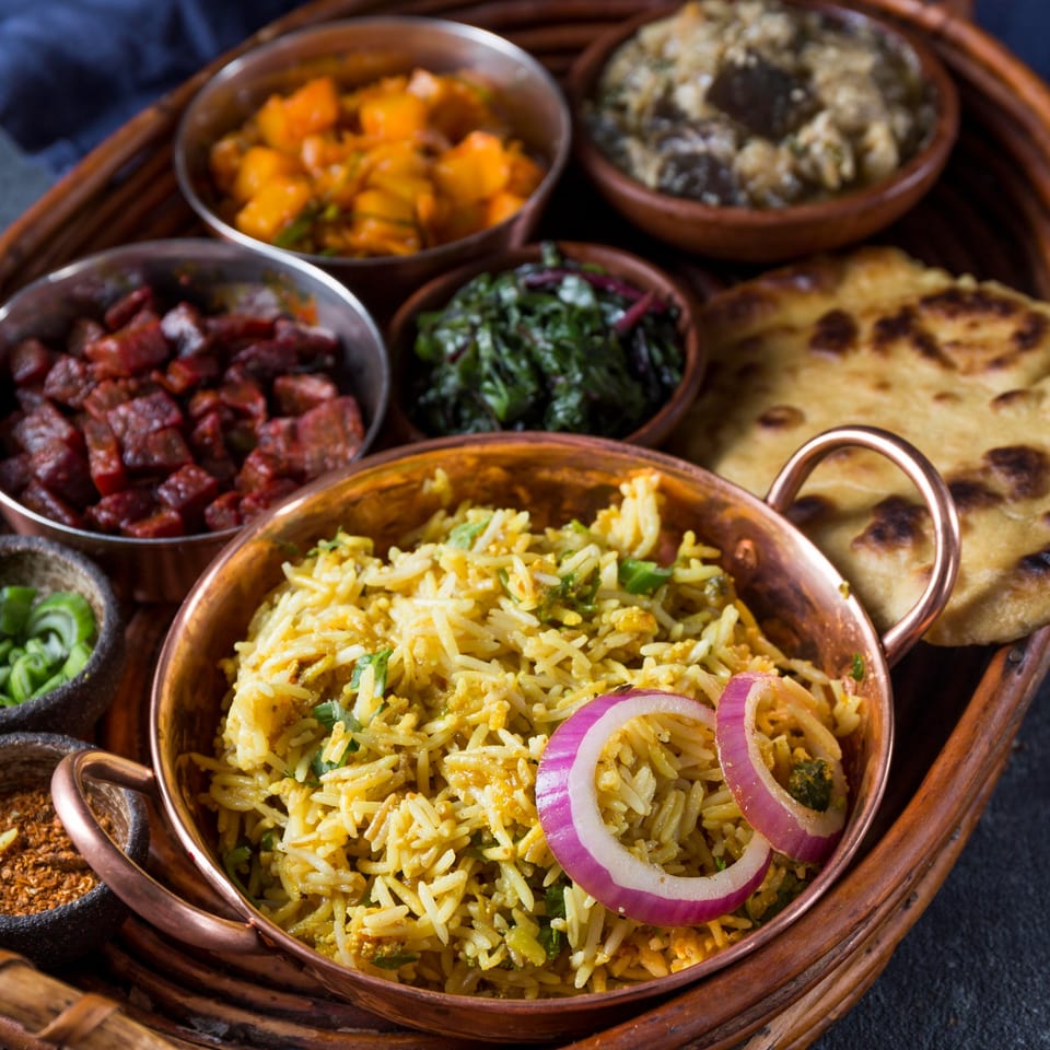 A Nepalese thali with rice, curries, flatbread, and spices served on a wooden tray.
